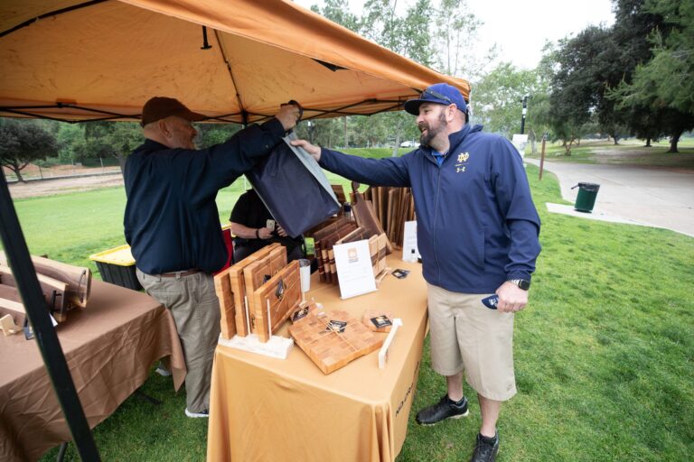 a man being handed a bag from another man in a tent with the David Lamb Woodworx logo on it