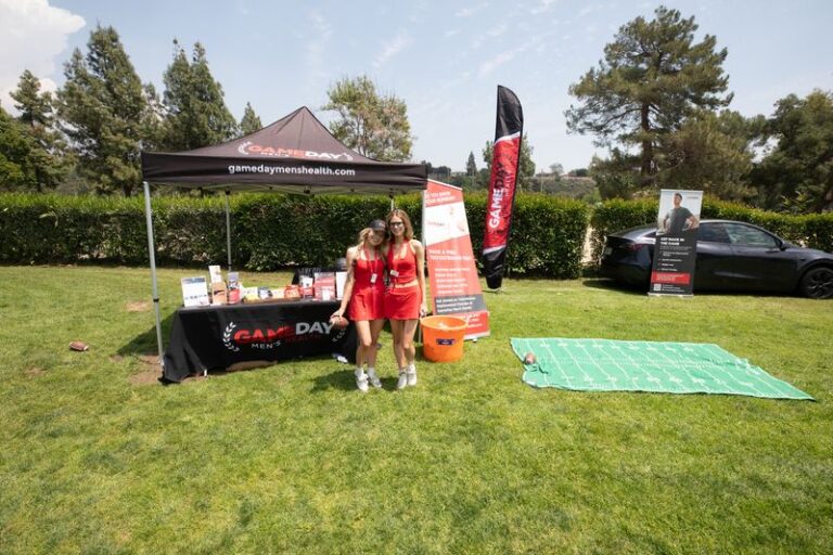 two girls in red dresses stand in front of a booth for Gameday Mens Health at a golf course