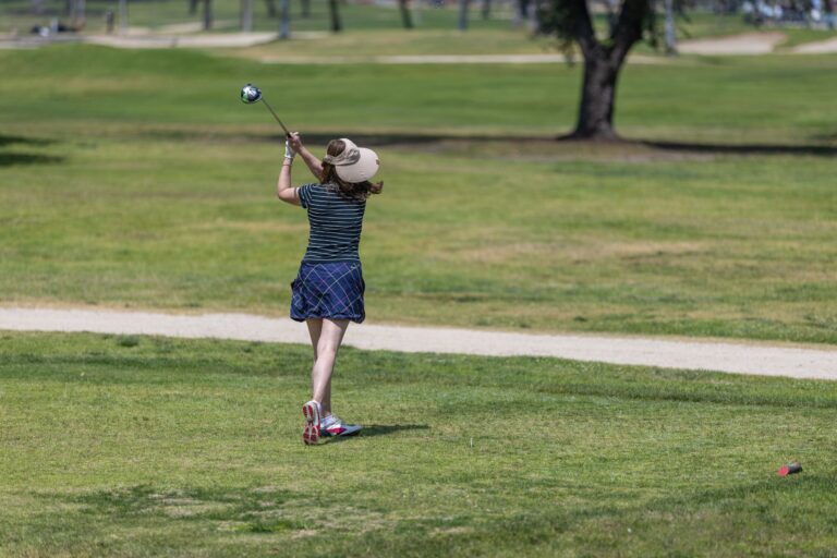 a woman in blue shorts and brown sunhat tees off at a golf course