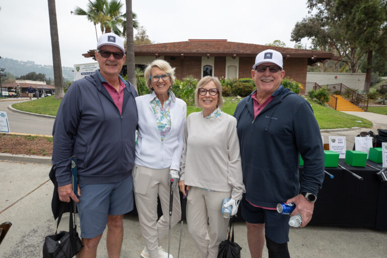 two women stand between two men posing at a golf course