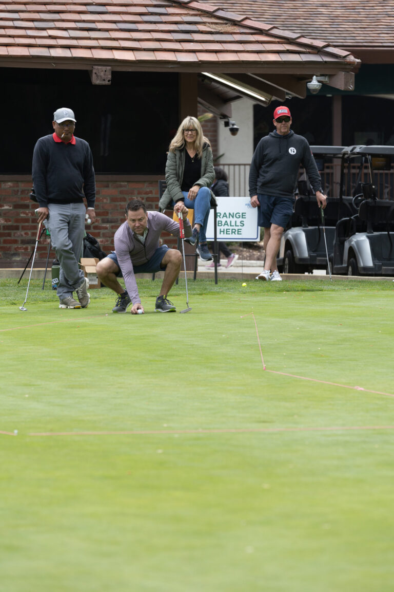 a man in gray crouches down to inspect a putt on a golf green