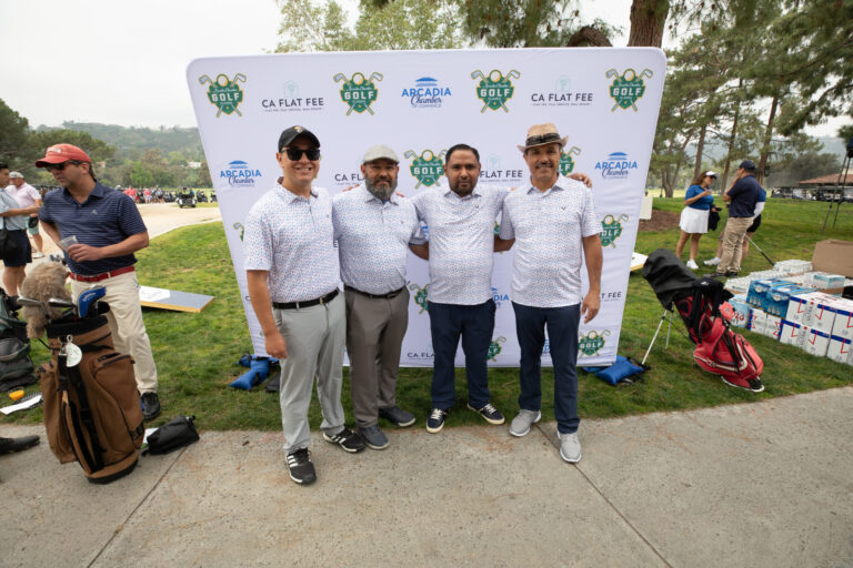 a group of four male golfers, all dress alike, pose in front of a step and repeat banner