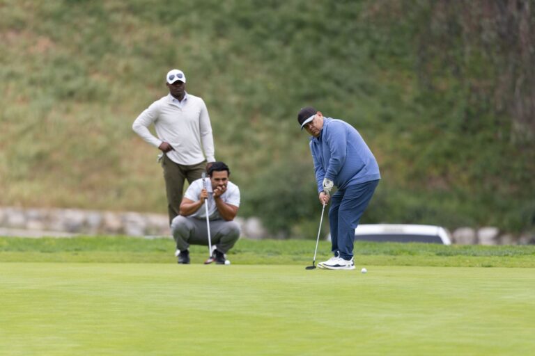 a man in all blue putts on a golf course while two other men look on