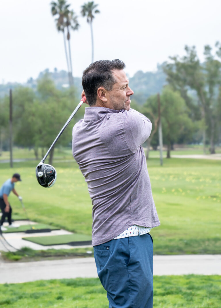 a man in a gray shirt hitting a golf ball