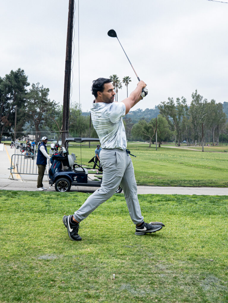 a man teeing off with a golf cart in the distance behind him