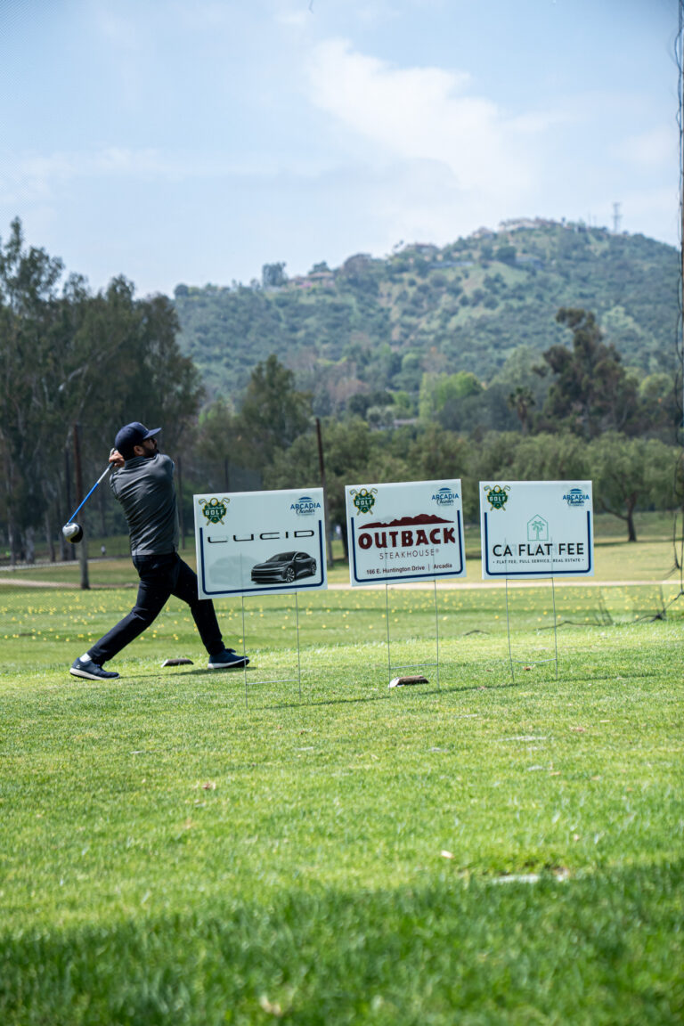 a golfer teeing off in front of three tee signs