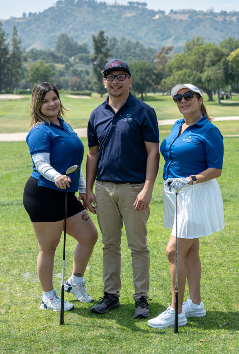 two women standing to either side of a man and all are wearing golf attire, to form the team for Foothill Credit Union