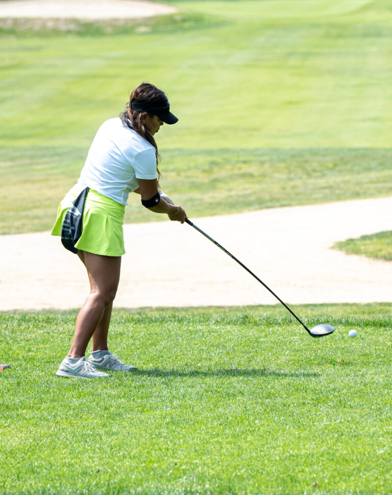a woman in a yellow skirt and white shirt hitting a golf ball near a sand trap