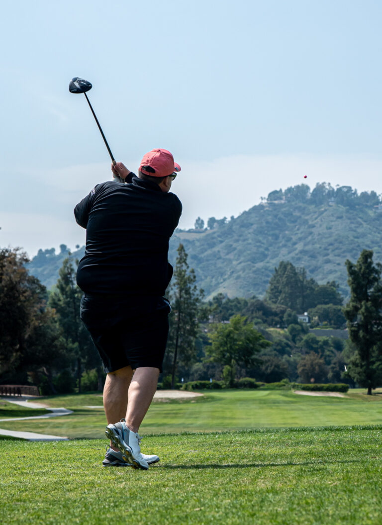a man in a black shirt and red hat teeing off