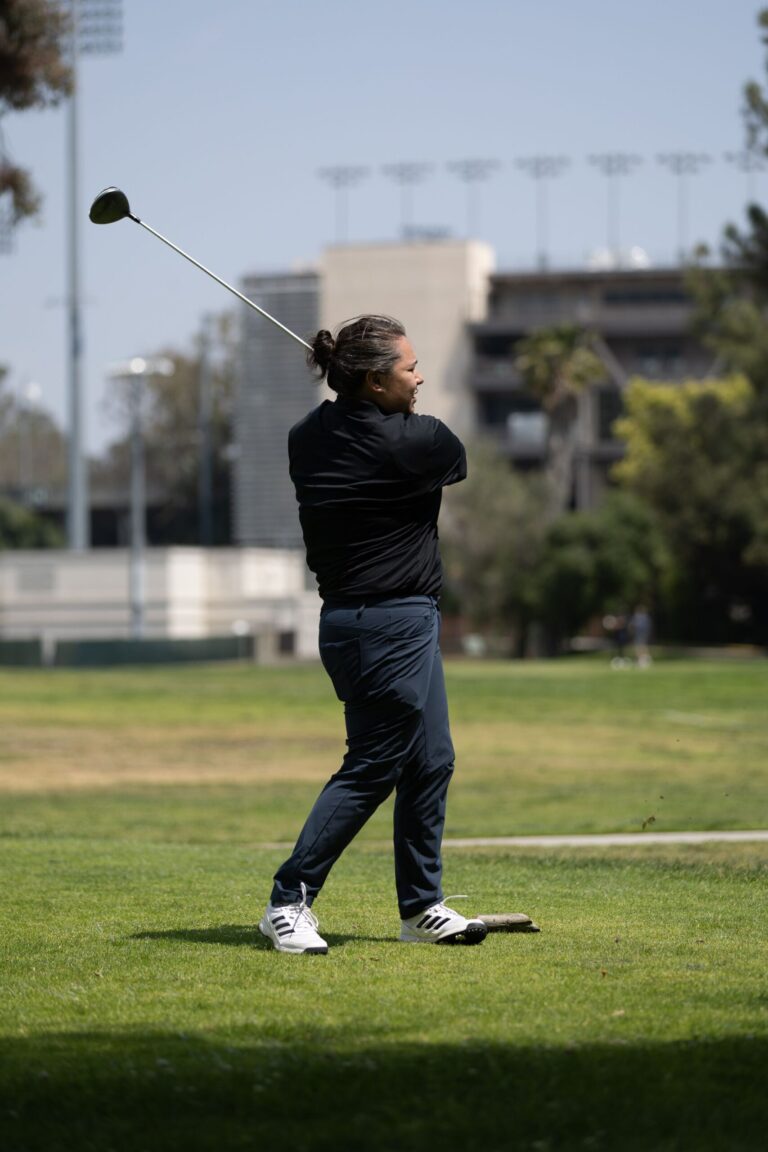 a man in all black tees off at a golf course with the Rose Bowl behind him
