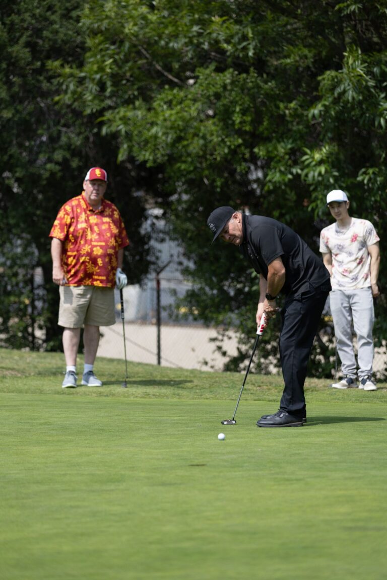 a man in black putts into a hole while two other men watch from behind him