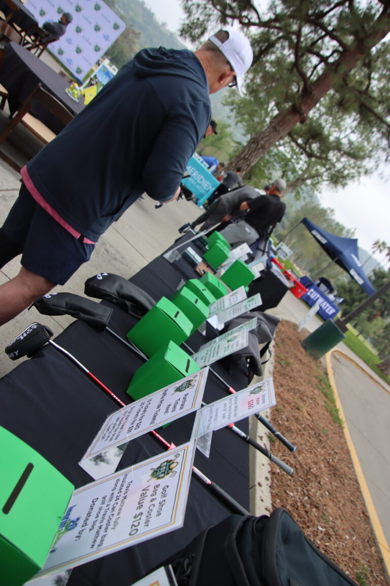 a man standing in front of a table of raffle prizes set with green boxes and signage