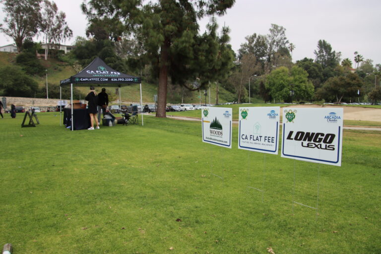 a line of tee signs on green grass with a CA Flat Fee tent in the background