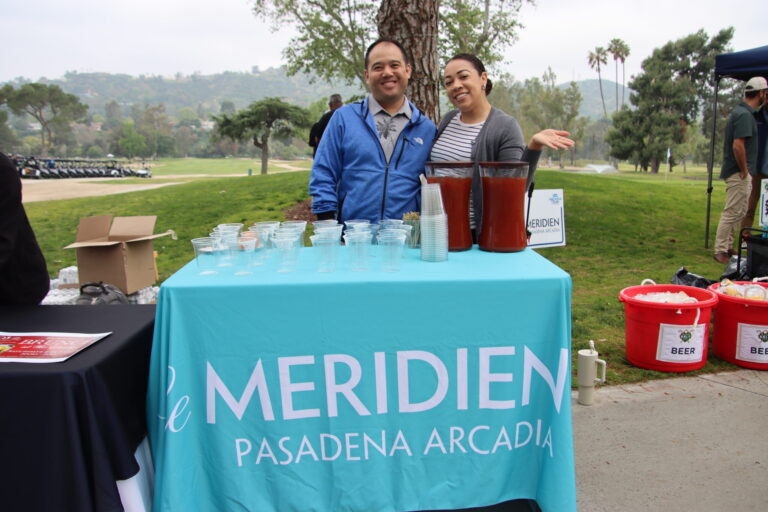 a woman and a man standing behind a table set with a light blue tablecloth with the Le Meridien logo on it
