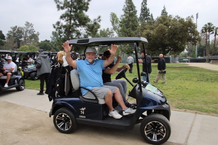 a man in a blue shirt waving his arms from a golf cart while the driver gives a thumbs up
