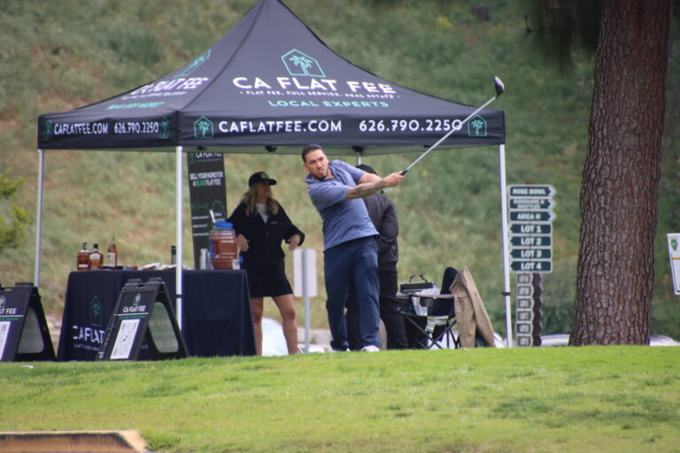 a man in a blue shirt teeing off in front of a CA Flat Fee tent