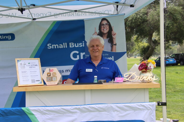 a man in a blue shirt standing behind a bar with a banner behind him from E-Marketing Associates