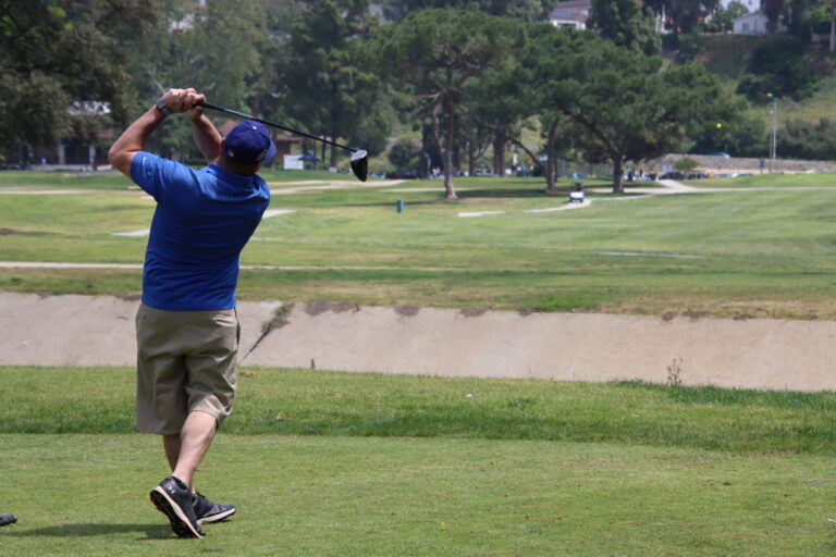 a man in a blue shirt and shorts teeing off over a large concrete ditch