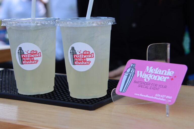 two cups full of lemonade stamped with the Redhead with a Shaker logo next to a pink business card for the same business