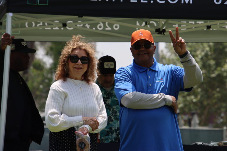 a woman in a white shirt smiling while a man beside her in a blue shirt gives a thumbs up
