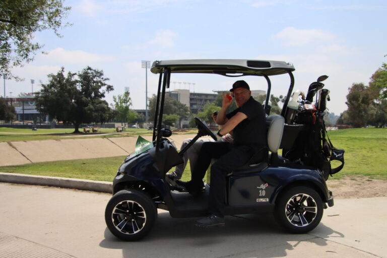 a man in a black shirt waving while driving a golf cart