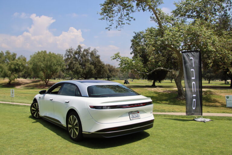 a white Lucid car on a golf course with trees and mountains as a backdrop