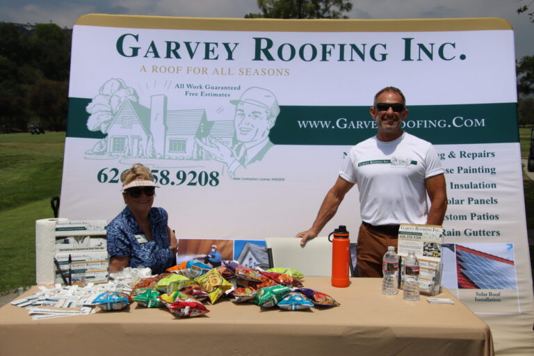 a woman seated with a man standing beside her and a Garvey Roofing banner behind them
