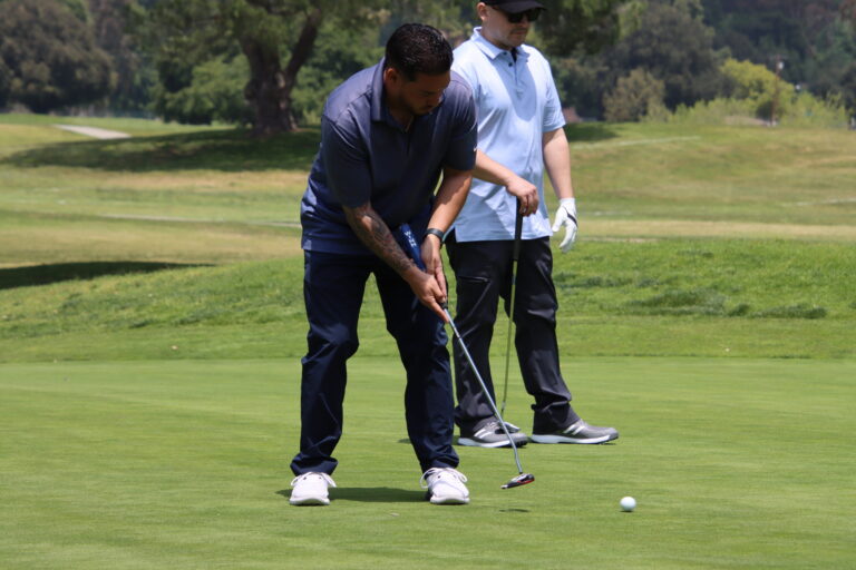 a man in a blue shirt and black pants putts a ball on a golf green