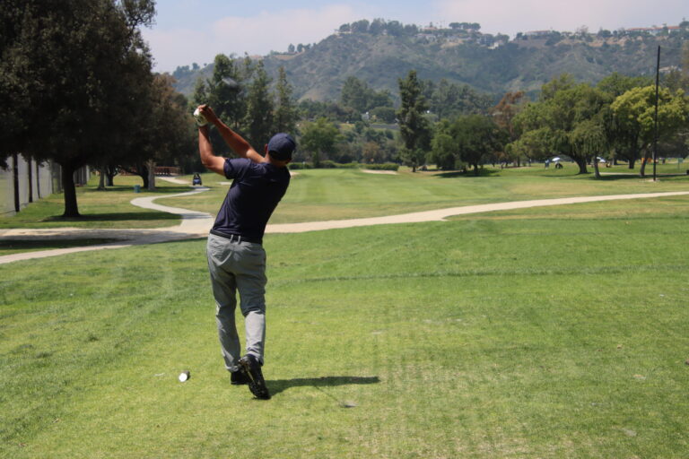 a man in gray pants and black shirt tees off towards a green hillside