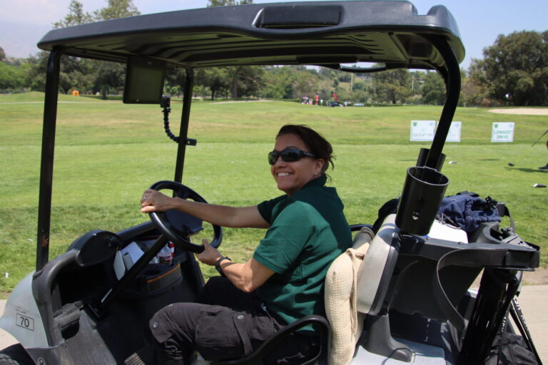 a woman in a green shirt driving a golf cart and turning towards the camera