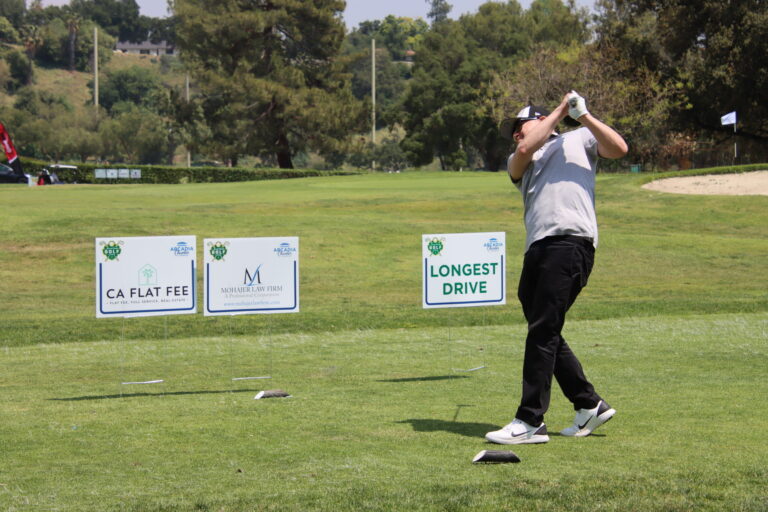 a man in a white shirt and black pants tees off in front of a grouping of tee signs, including on that reads Longest Drive Contest