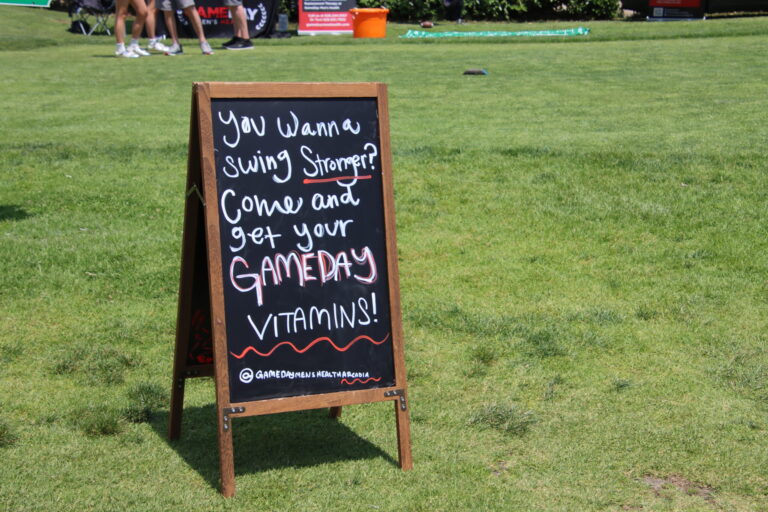 an A Frame sign from Gameday set on green grass, reading you wanna swing stronger? Come and get your Gameday vitamins.