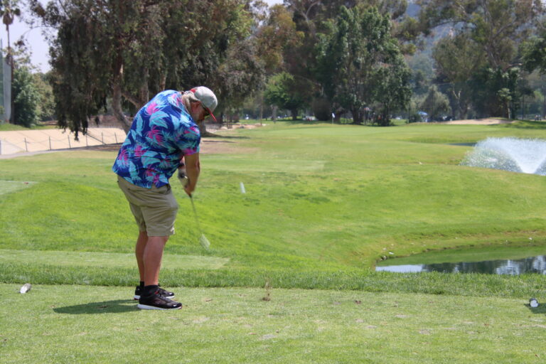 a man in a colorful shirt hits a ball towards a water feature on a golf course