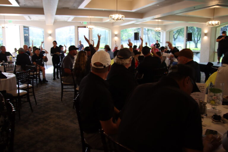 a group of people seated at tables in a banquet hall holding their arms up in the air
