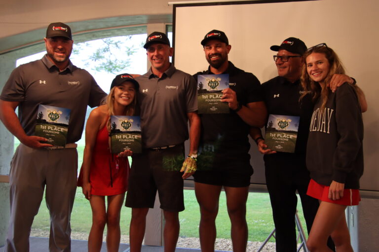 a group of people standing in front of a projector screen holding awards from a golf tournament