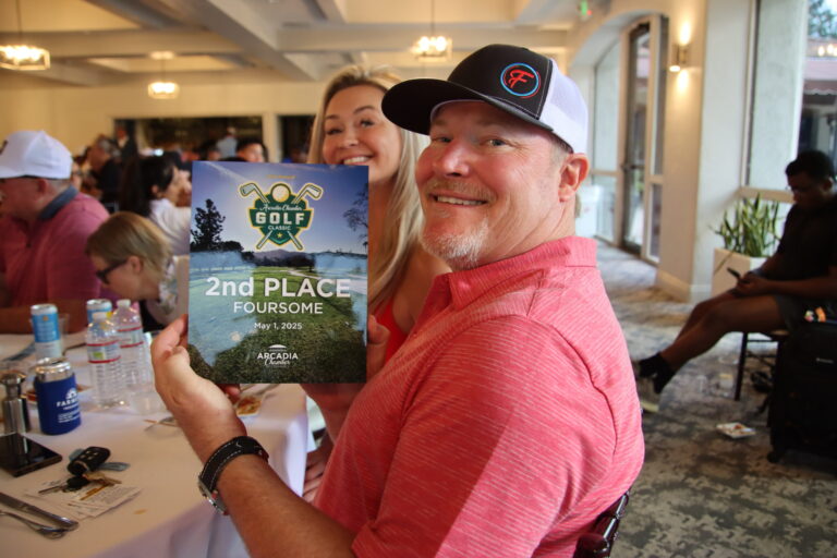 a man in a pink shirt holding up a plaque for second place for foursomes at the Arcadia Chamber golf tournament