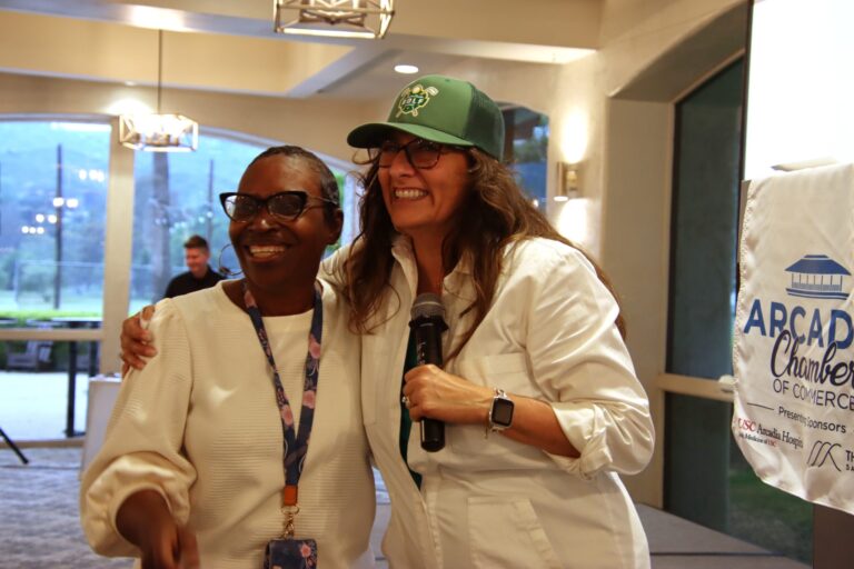 two women, both wearing white, smiling, with a podium showing the Arcadia Chamber logo behind them