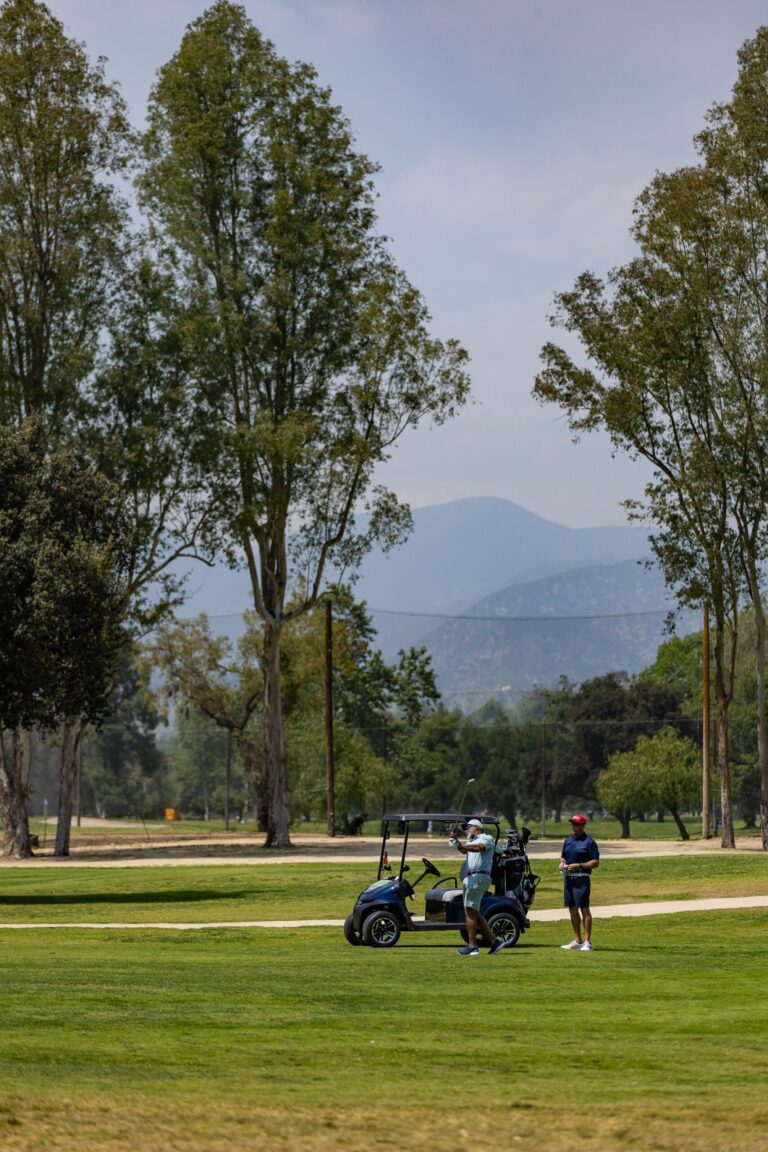 a group of golfers standing beside their golf cart with the mountains in the distance