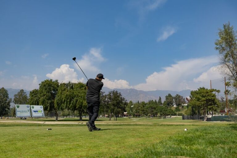 a man all in black tees off with blue skies and mountains in the distance