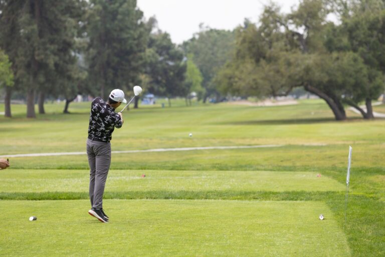 a man in a black patterned shirt tees off at a golf course