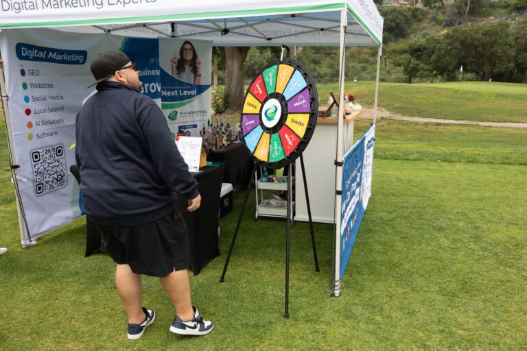 a man in black stands in front of a spinning wheel and tent for E-Marketing Associates