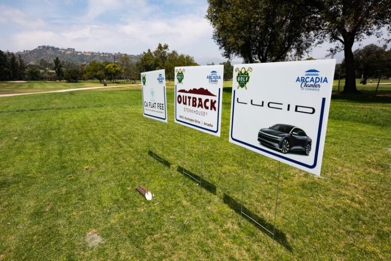 a row of golf tee signs with logos for Lucid and Outback