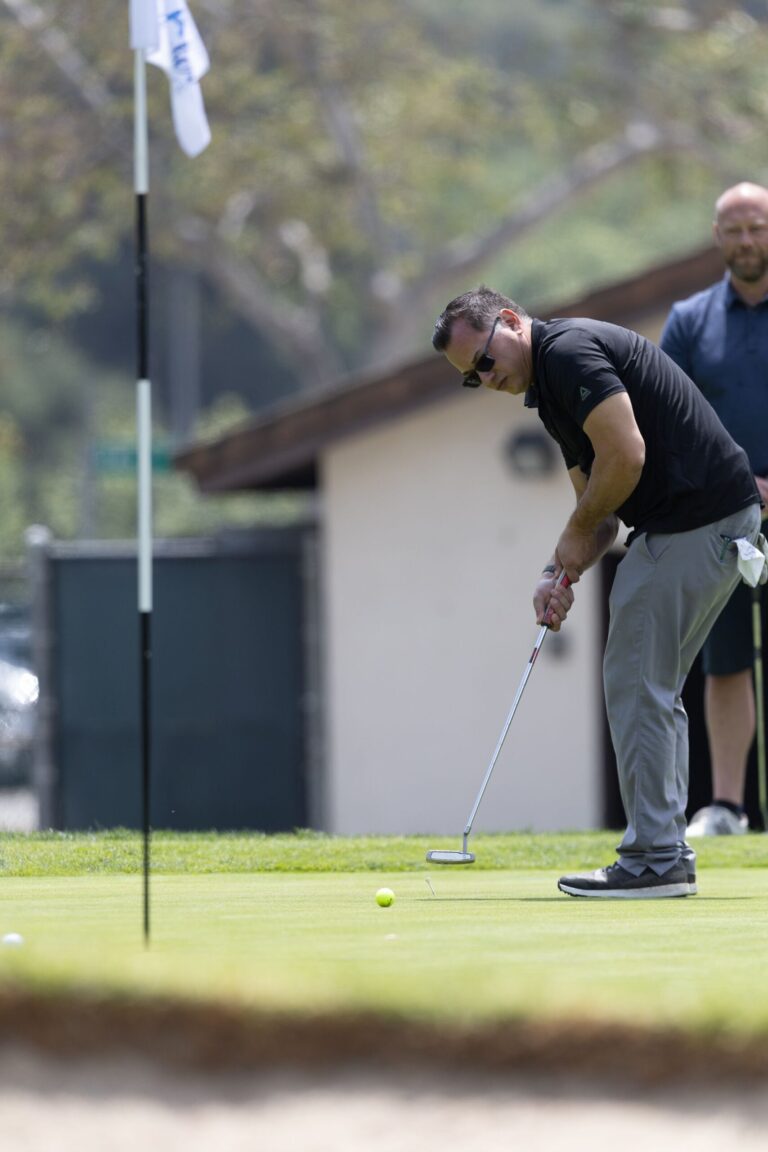 a man in a black shirt and gray pants putts a ball into a hole