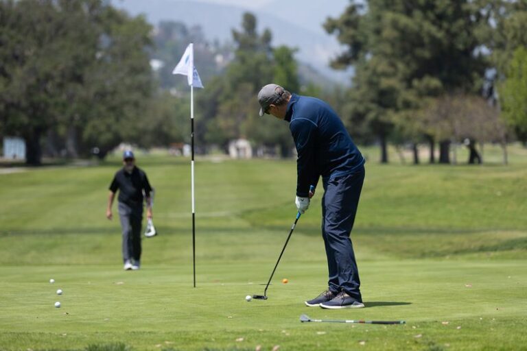 a man in a blue shirt posed to hit a golf ball into the hole