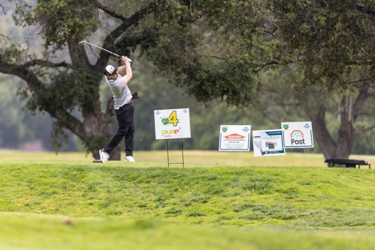a man tees off next to a row of golf tee signs