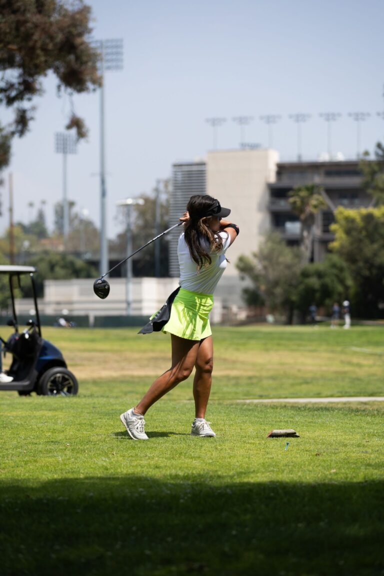 a woman in a yellow golf skirt tees off at a golf course