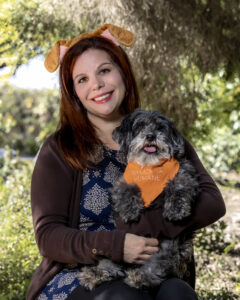 a woman holding a cute gray dog wearing an orange bandana 