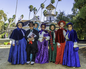 carolers in front of the Queen Anne Cottage at the LA Arboretum 