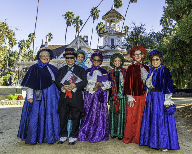 Carolers carolers in front of the Queen Anne Cottage at the LA Arboretum