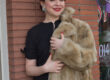 a woman in a black dress holds a fur coat while leaning on a brick wall